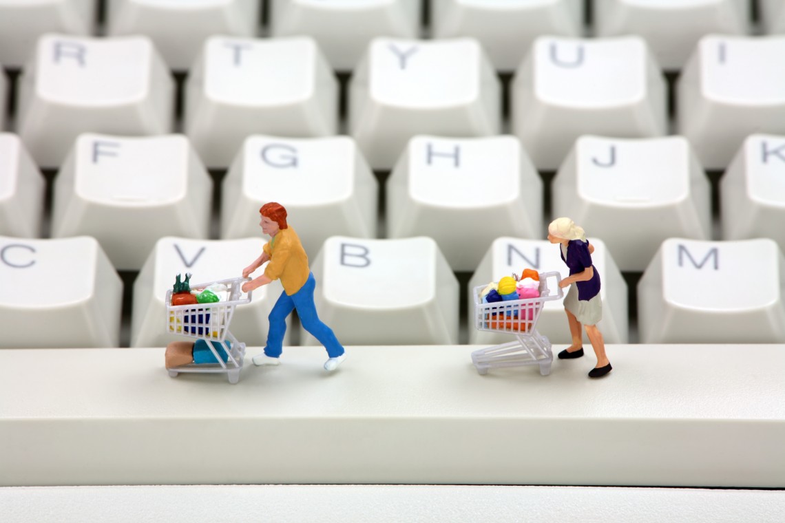 Miniature shoppers with shopping carts on a computer keyboard. Online shopping concept.